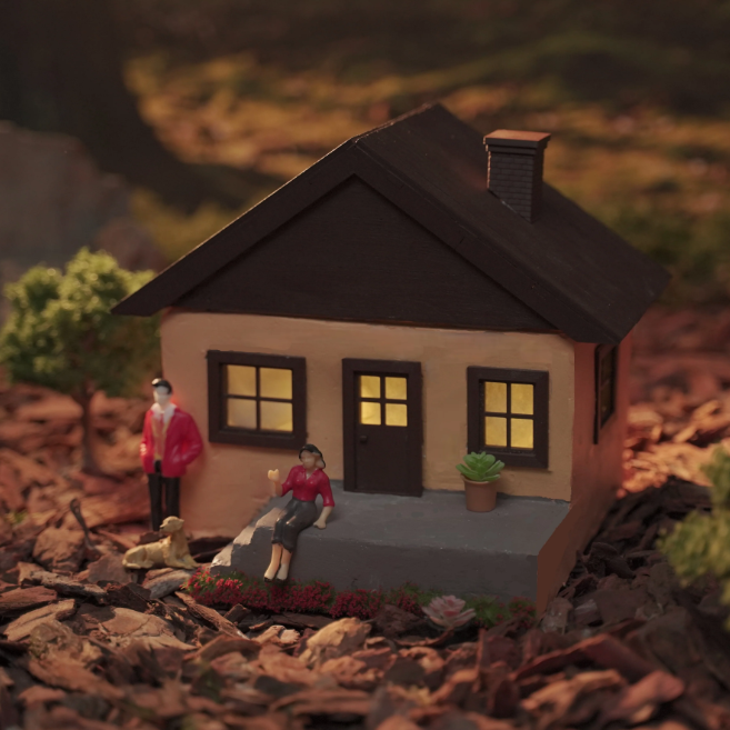 Miniature concrete house with mini family figures and plants in a cozy evening scene